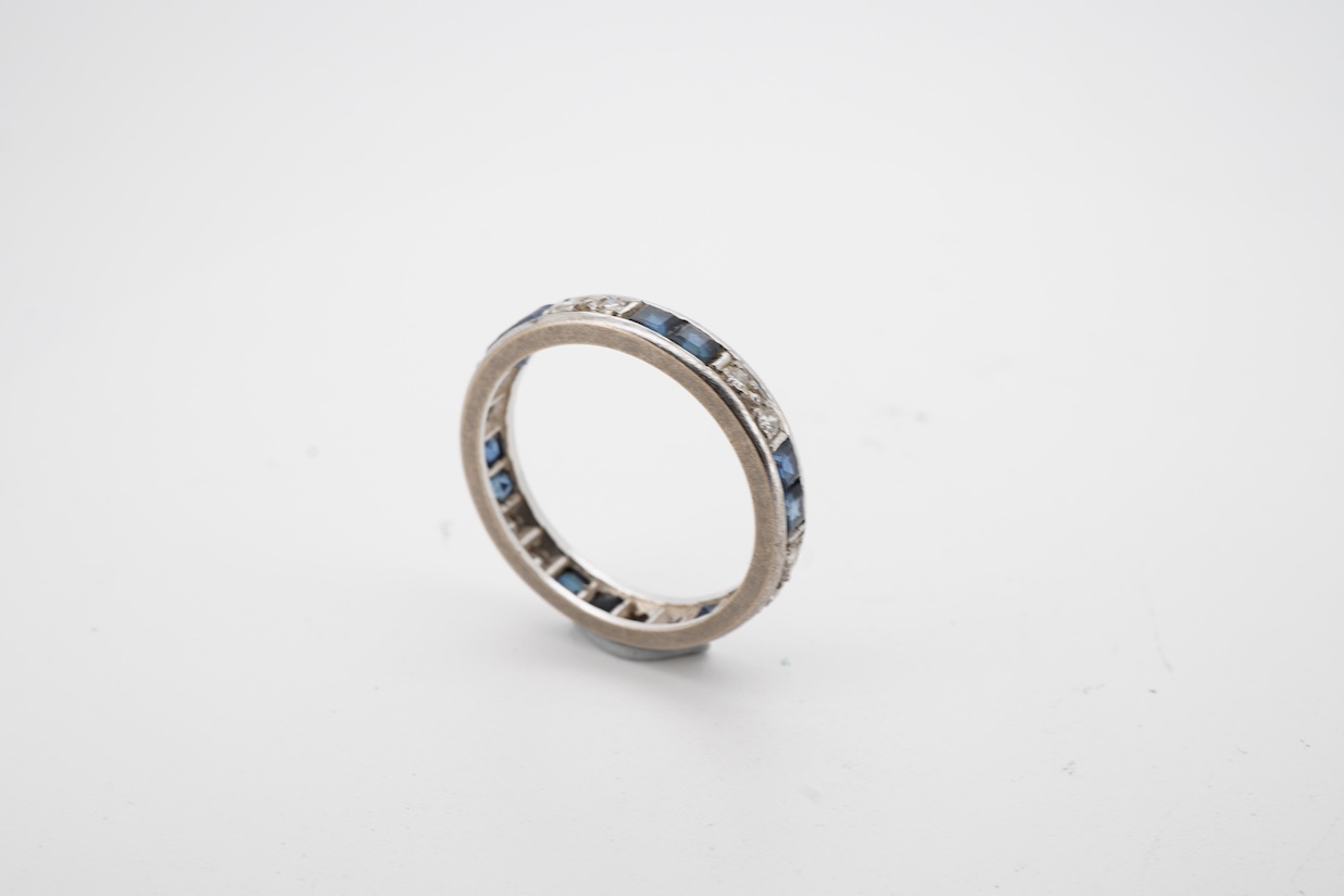 A white metal, twelve stone diamond and twelve stone sapphire set full eternity ring, size N, (remnants of an 18ct hallmark?).